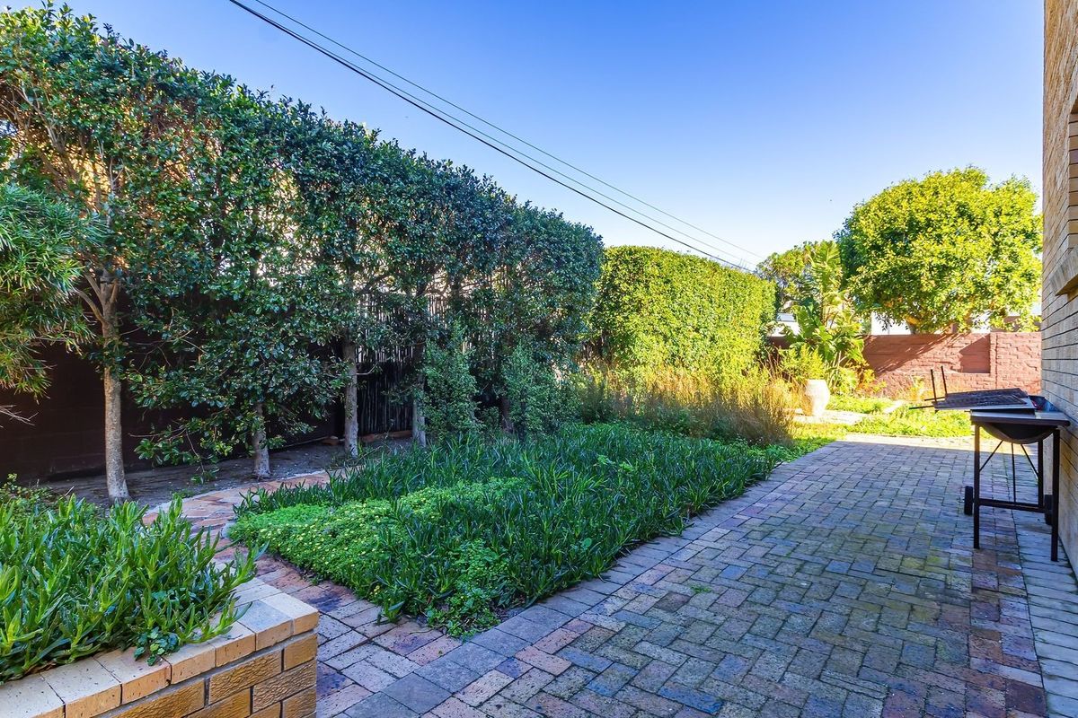 A well-maintained rear garden area featuring brick paving, a structured brick planter box, and established privacy hedging along the boundary.
