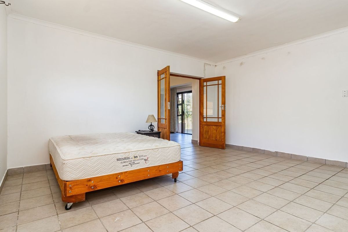 Spacious bedroom featuring tiled flooring, neutral walls, and wooden double doors leading to an adjacent living area.