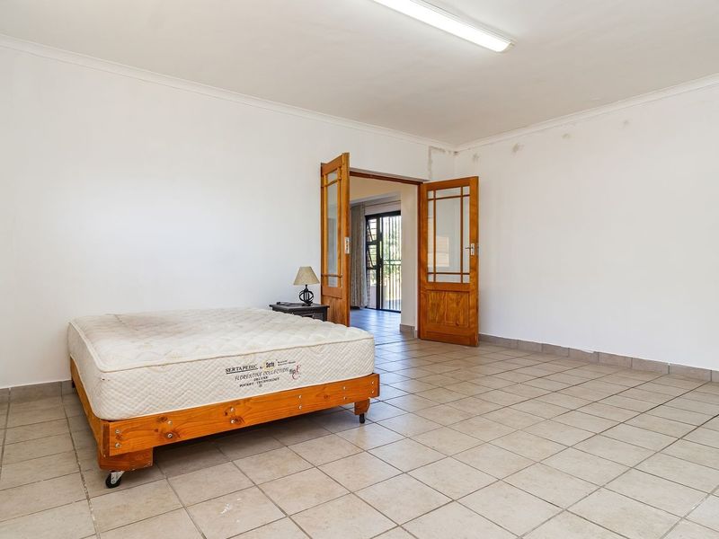 Spacious bedroom featuring tiled flooring, neutral walls, and wooden double doors leading to an adjacent living area.