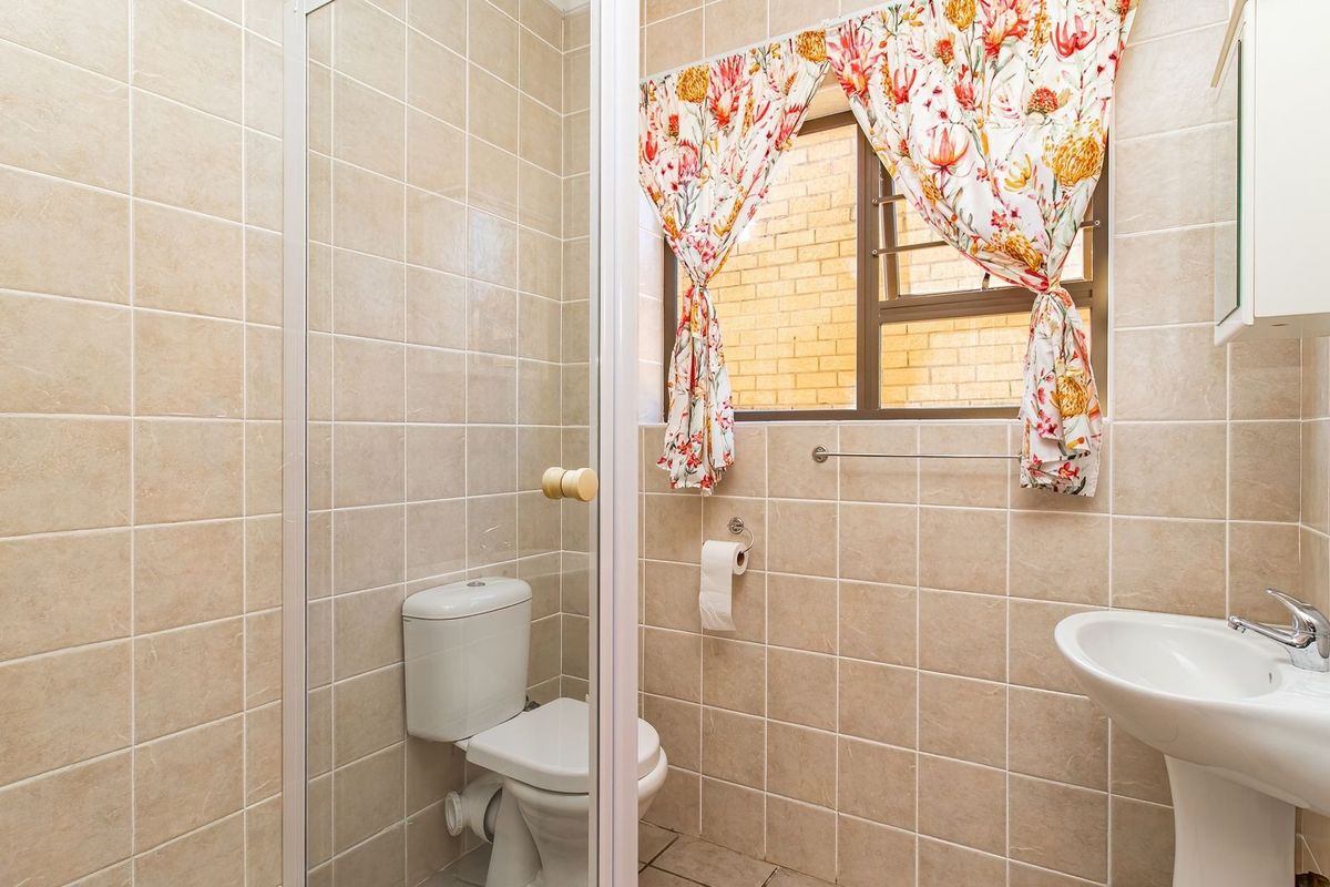 A functional bathroom featuring a pedestal basin, toilet, and a glass-enclosed shower, finished with neutral wall and floor tiling.