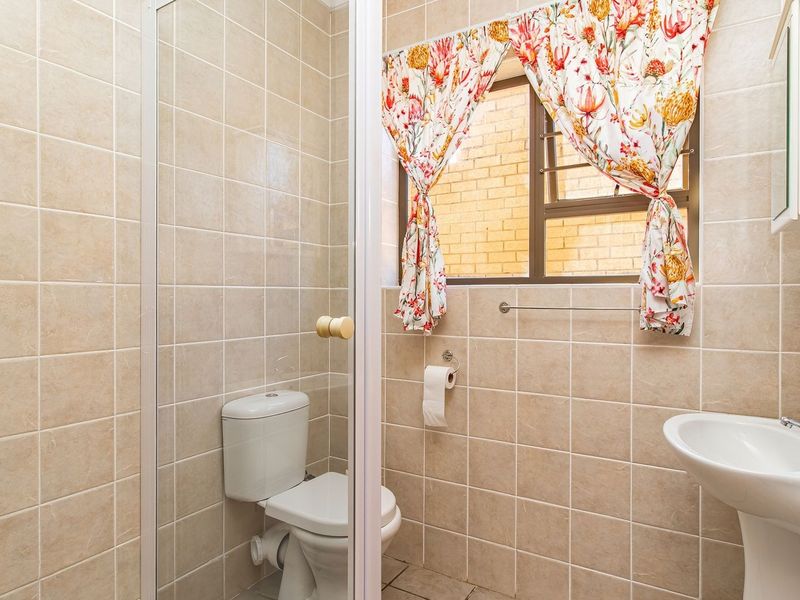 A functional bathroom featuring a pedestal basin, toilet, and a glass-enclosed shower, finished with neutral wall and floor tiling.