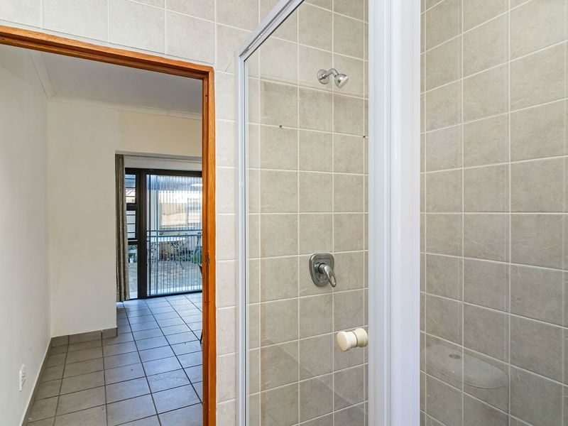 A functional bathroom featuring a glass-enclosed shower with neutral wall tiling and tiled flooring, providing a clean and practical space.