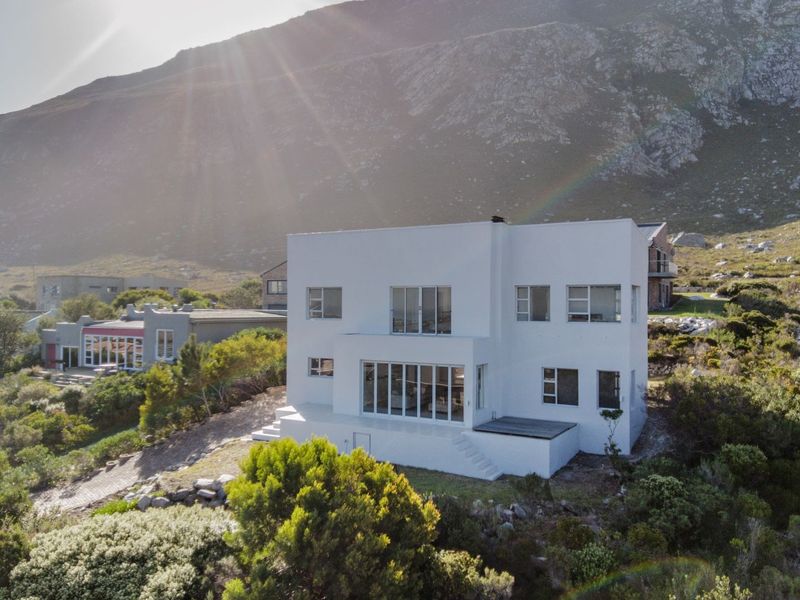 Aerial view of a modern white multi-story residential property set against a mountain backdrop, featuring clean lines and large windows.