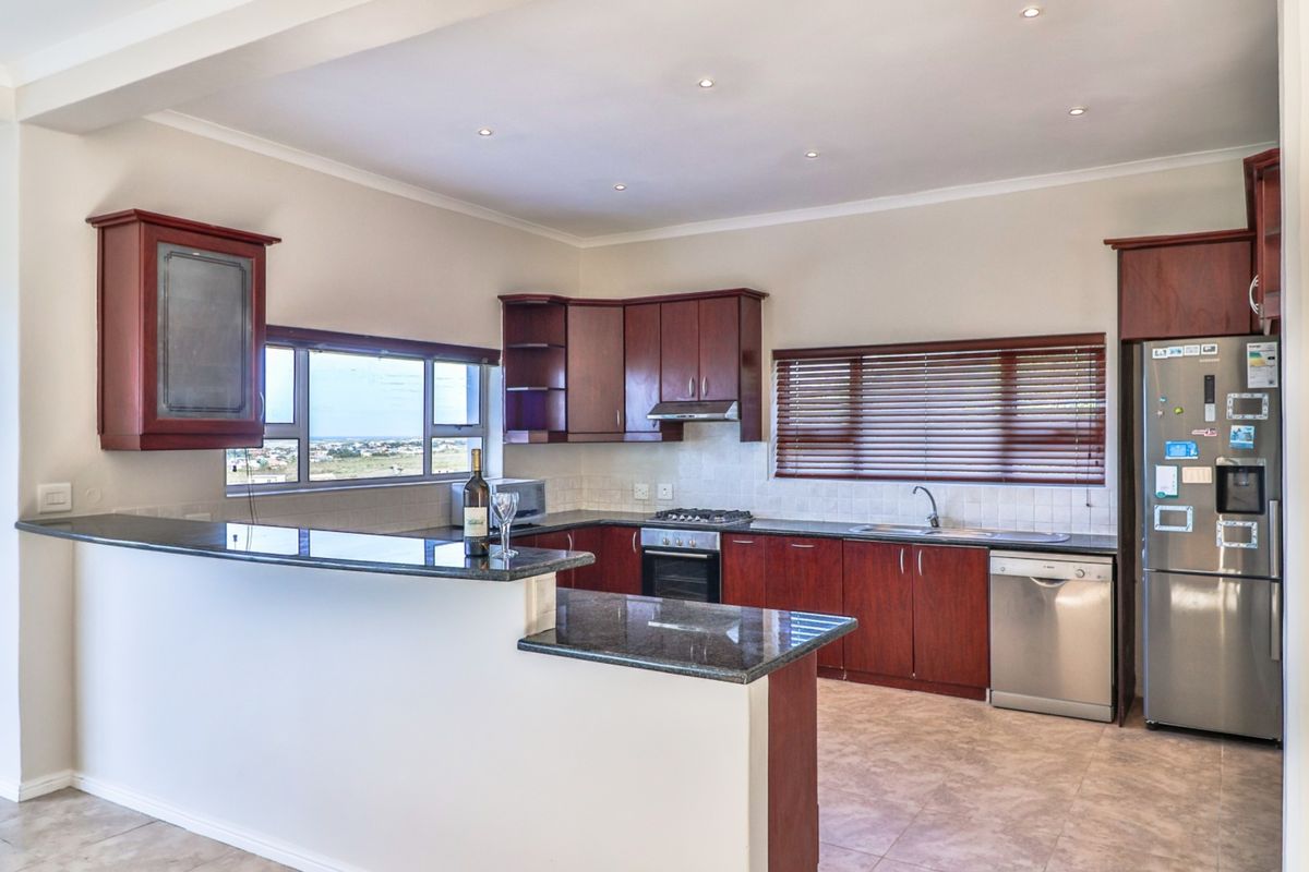 A functional kitchen featuring dark wood cabinetry, granite countertops, a gas hob, and integrated appliances, with a breakfast bar overlooking the living area.