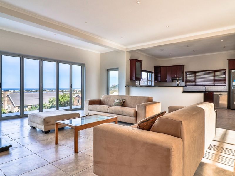 Spacious open-plan living area featuring tiled floors, recessed lighting, and large aluminium stacker doors leading to a scenic view, adjacent to a functional kitchen.