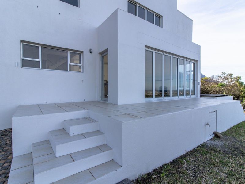 Rear exterior view of the property featuring a tiled patio, bi-fold doors, and concrete steps leading to the garden area.