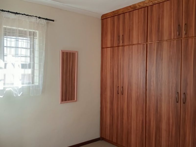 A bedroom featuring floor-to-ceiling built-in wooden wardrobes and a window fitted with security bars.