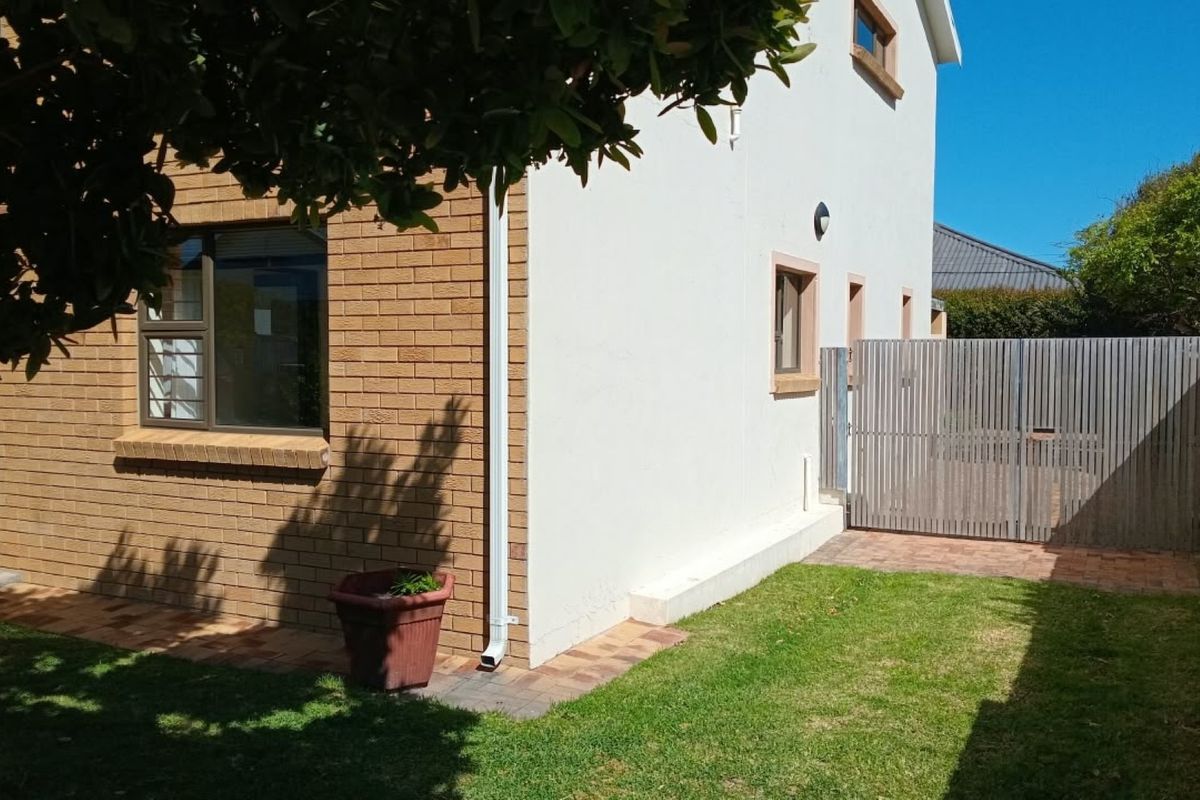 Rear exterior view of the apartment featuring a combination of brick and plastered walls, paved pathways, and a secure timber gate leading to the garden.