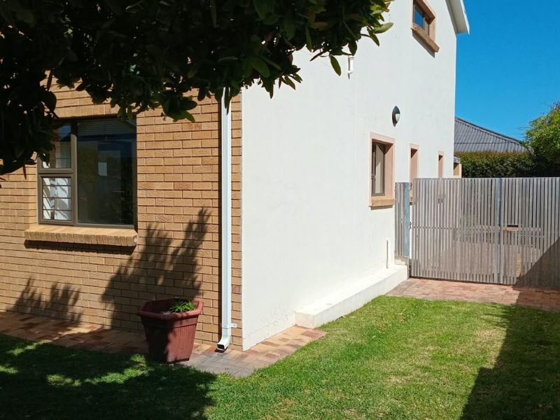 Rear exterior view of the apartment featuring a combination of brick and plastered walls, paved pathways, and a secure timber gate leading to the garden.