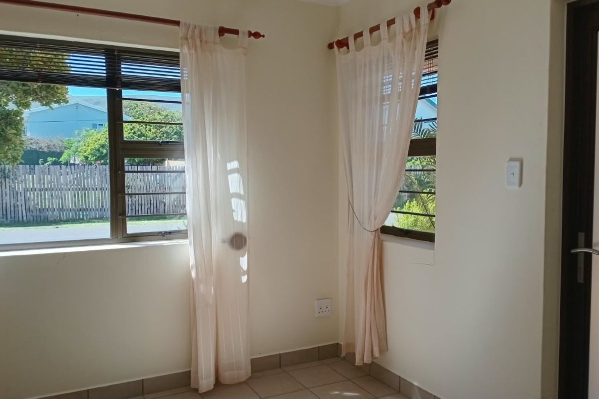A bright, empty bedroom featuring tiled flooring, neutral walls, and aluminium windows with security bars, offering a clean canvas for personalization.