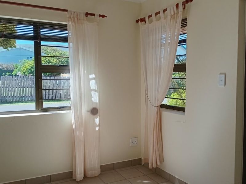 A bright, empty bedroom featuring tiled flooring, neutral walls, and aluminium windows with security bars, offering a clean canvas for personalization.