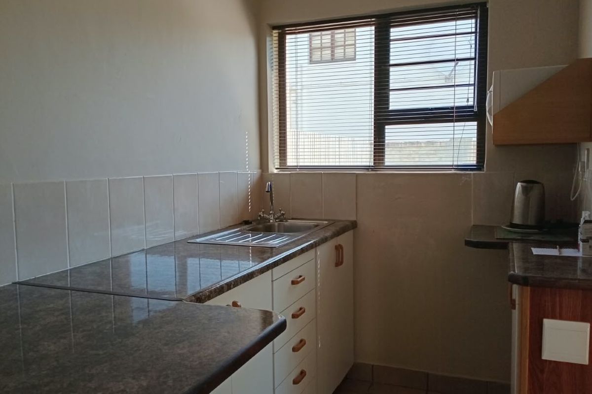 A functional kitchen area featuring laminate countertops, a stainless steel sink with mixer tap, tiled splashbacks, and built-in cabinetry.