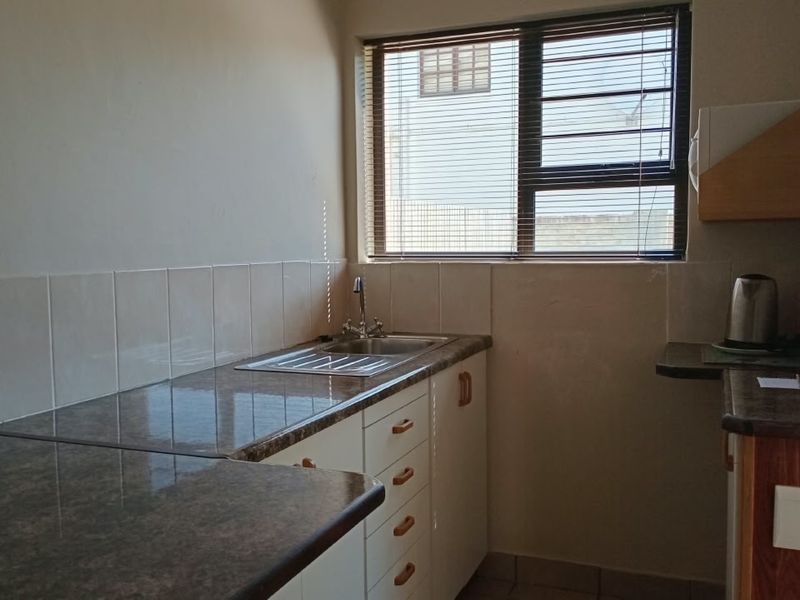 A functional kitchen area featuring laminate countertops, a stainless steel sink with mixer tap, tiled splashbacks, and built-in cabinetry.