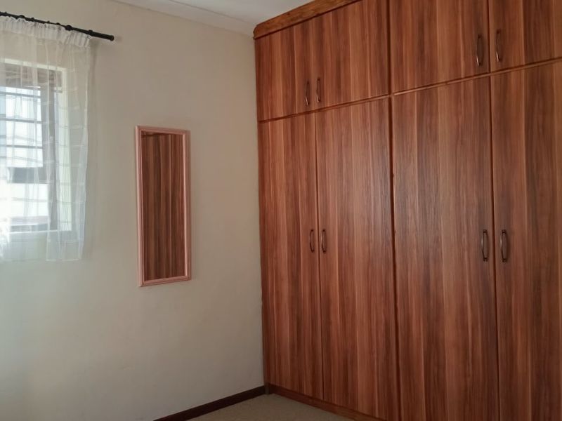 A clean bedroom featuring extensive floor-to-ceiling built-in wooden cupboards and a window with natural light.