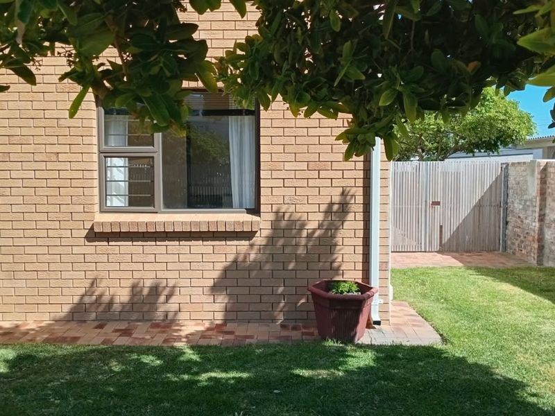 A well-maintained rear exterior view featuring a face brick facade, paved patio area, and a private garden with a timber gate.
