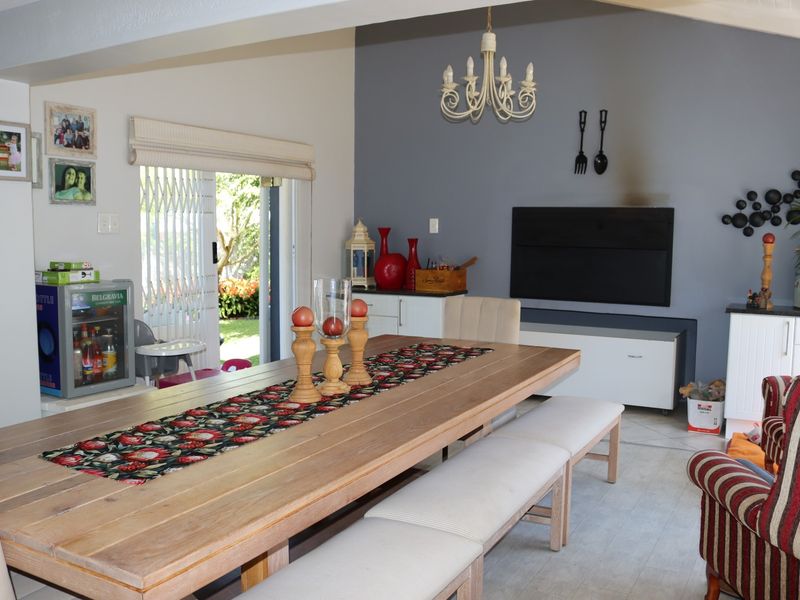 Spacious open-plan living and dining area featuring tiled flooring, a chandelier, and direct access to the garden through a sliding glass door.