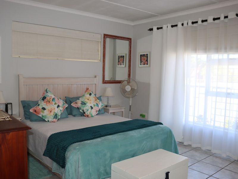 A well-lit bedroom featuring tiled flooring, neutral wall tones, and a window fitted with security bars and curtain fixtures.