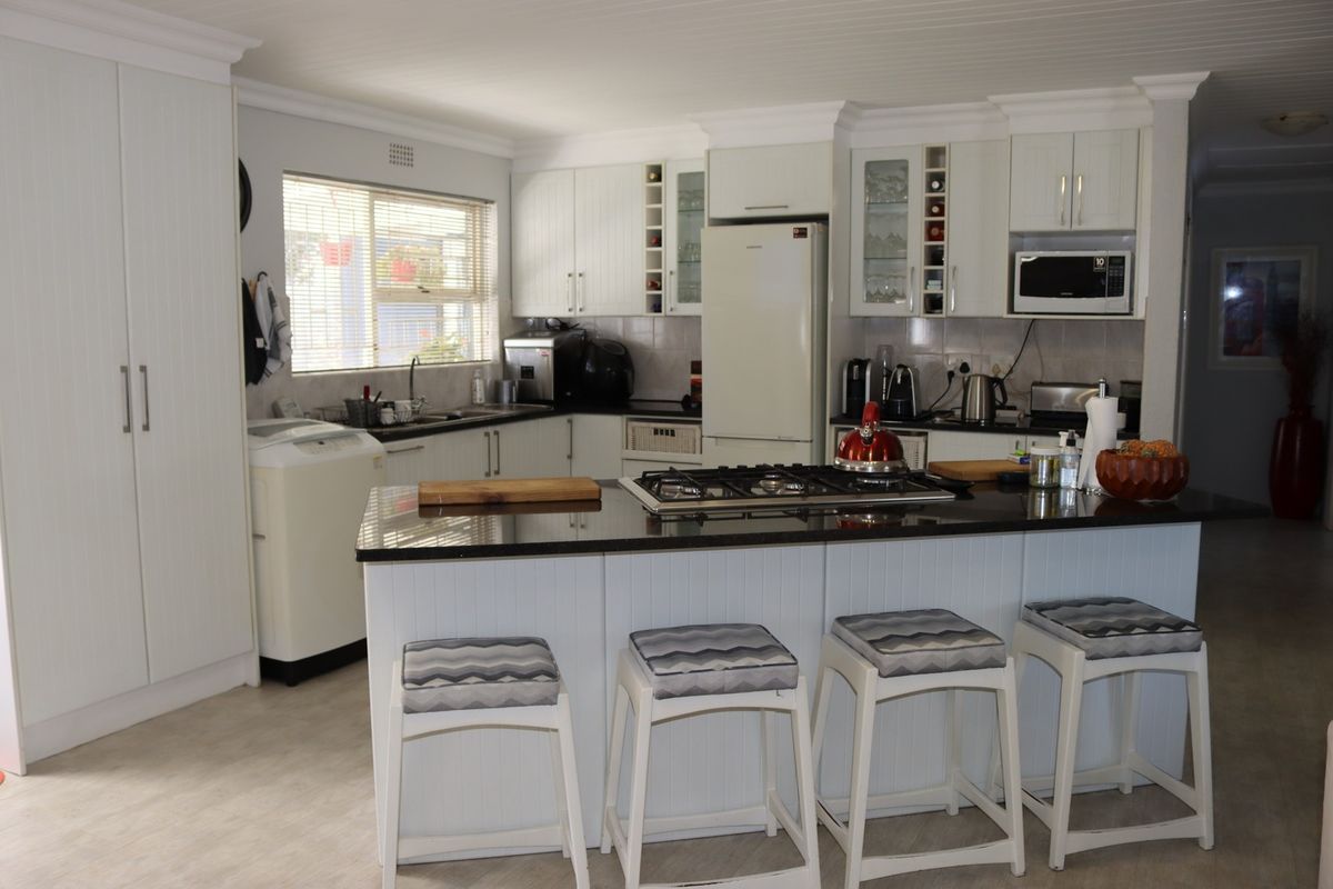 A well-maintained kitchen featuring white cabinetry, granite countertops, a central island with a gas hob, and integrated appliances.