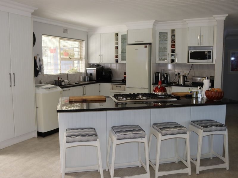 A well-maintained kitchen featuring white cabinetry, granite countertops, a central island with a gas hob, and integrated appliances.