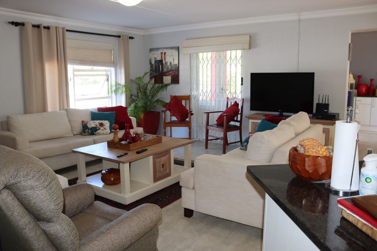 A comfortable living room featuring neutral walls, window blinds, and a security gate leading to the exterior.