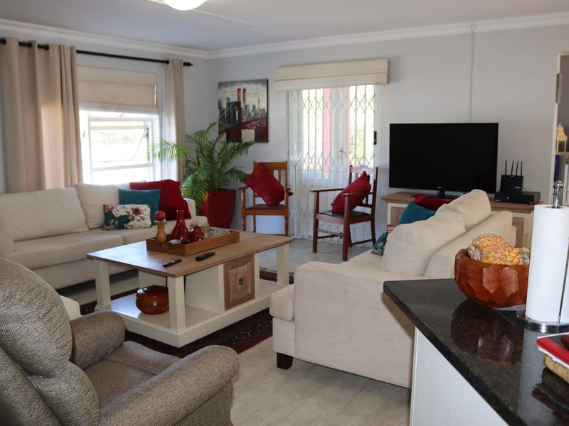 A comfortable living room featuring neutral walls, window blinds, and a security gate leading to the exterior.