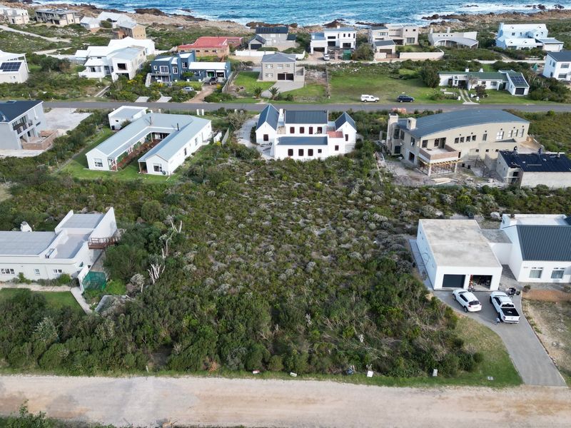 Aerial view of a vacant residential plot situated in a coastal neighborhood, surrounded by established homes and natural vegetation.