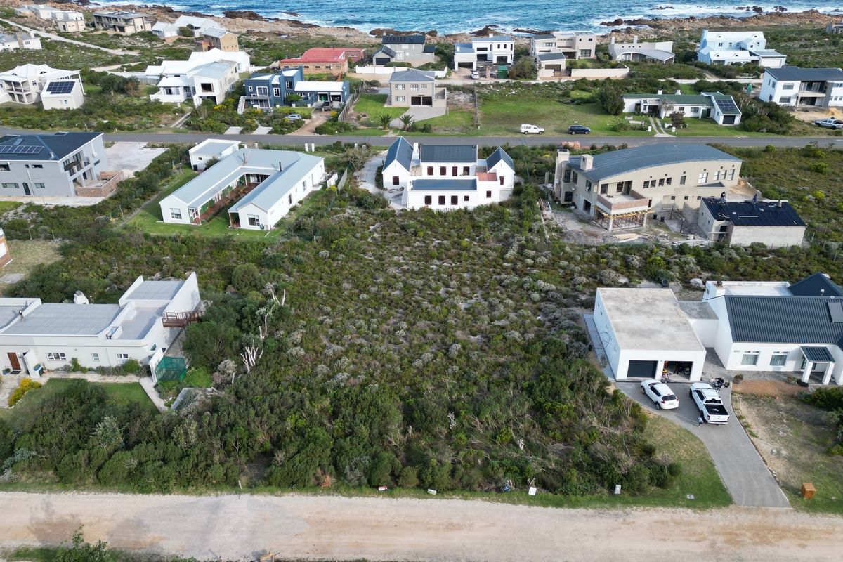 Aerial view of a vacant residential plot situated in a coastal neighborhood, surrounded by established homes and natural vegetation.