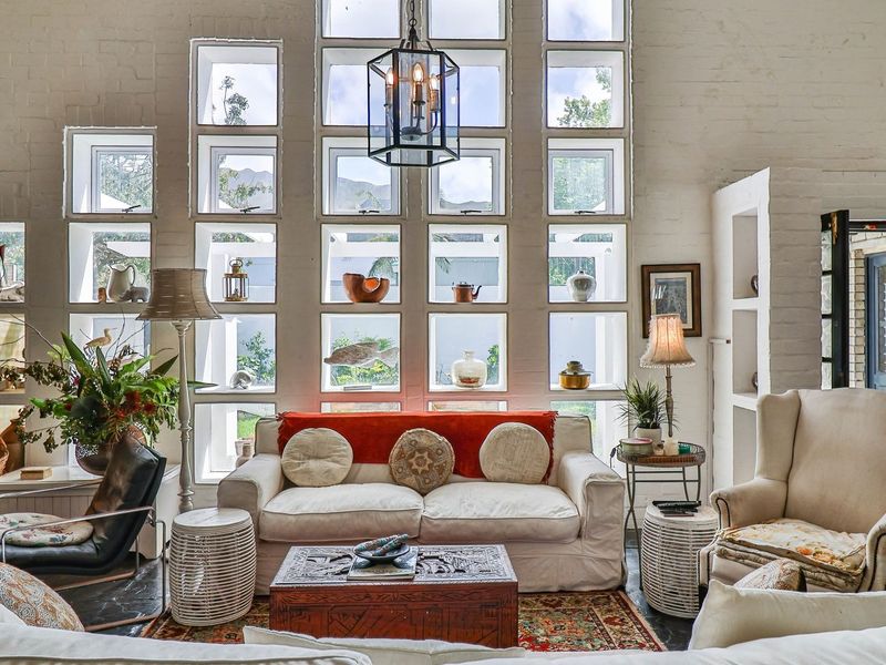 A bright living room featuring a striking grid-pattern window wall, exposed brickwork, and stone flooring, creating a unique and character-filled living space.