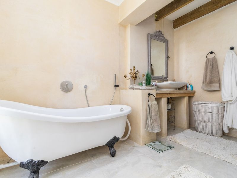 A charming bathroom featuring a classic clawfoot bathtub, a rustic vessel sink vanity, and exposed timber ceiling beams with warm plaster wall finishes.