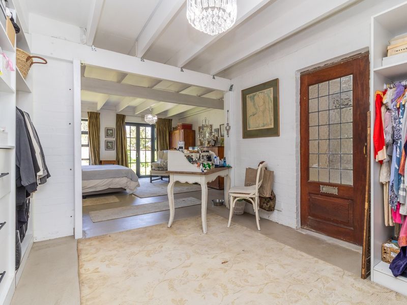 Spacious bedroom featuring exposed ceiling beams, painted brick walls, and built-in storage, with an adjoining living area visible through the open transition.