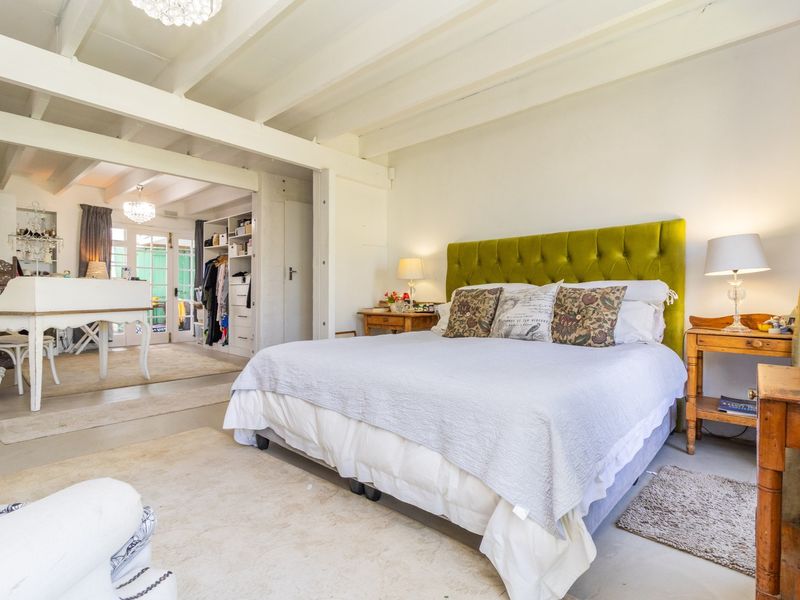 Spacious bedroom featuring exposed white ceiling beams, integrated storage shelving, and direct access to an adjoining area through glass-paned doors.