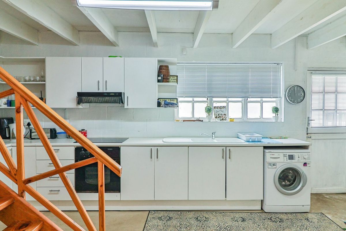 A functional kitchen featuring white cabinetry, built-in appliances, exposed beam ceilings, and a stable door, with an adjacent timber staircase.
