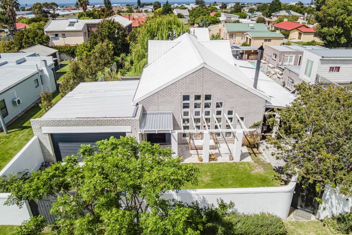Aerial view of a modern brick house featuring a metal roof, attached garage, and a pergola-covered patio area within a landscaped garden.