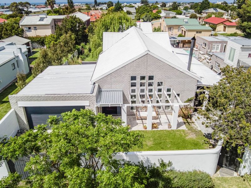 Aerial view of a modern brick house featuring a metal roof, attached garage, and a pergola-covered patio area within a landscaped garden.