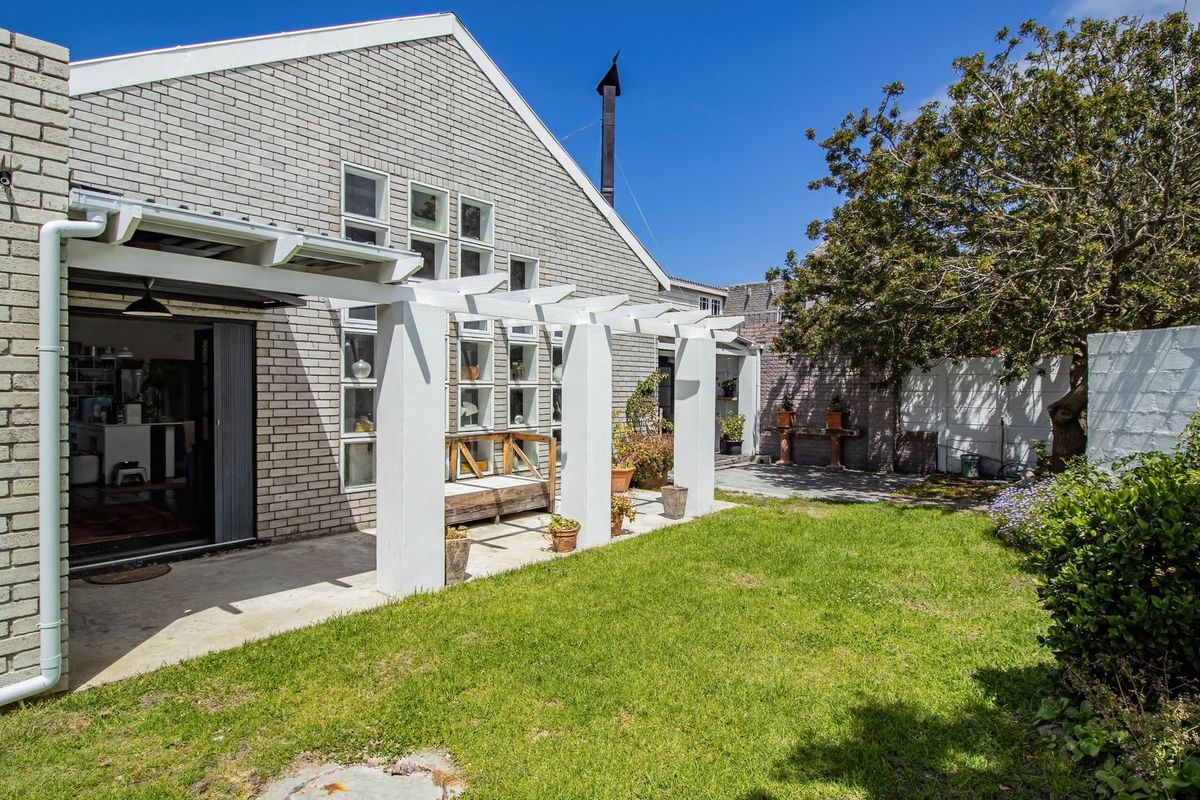 Rear view of the property featuring a white pergola, concrete patio area, and a well-maintained garden with a brick facade.
