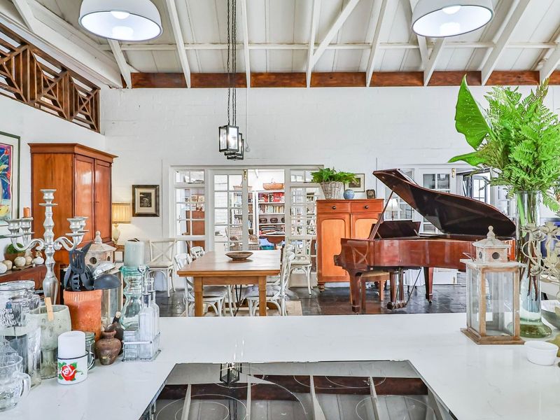 Spacious open-plan living and dining area featuring vaulted ceilings with exposed timber beams, painted brick walls, and direct access through classic french doors.