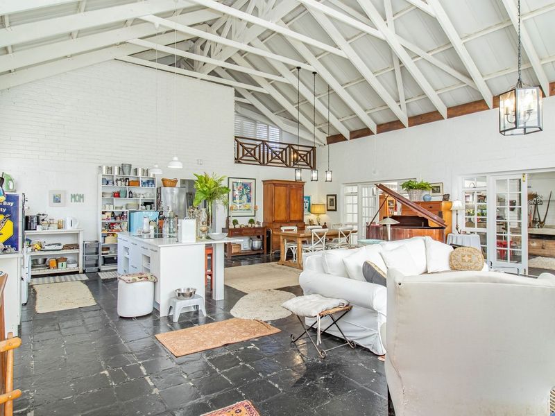 Spacious open-plan living area featuring high vaulted ceilings with exposed beams, painted brick walls, and dark stone flooring, creating a bright and airy atmosphere.
