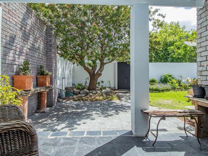 A covered patio area featuring brick walls and stone paving, overlooking a private garden with mature trees and landscaped borders.