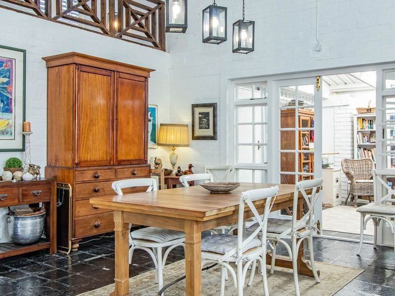 A bright dining room featuring exposed white brick walls, dark slate flooring, and timber ceiling beams, with direct access to an adjoining patio area.