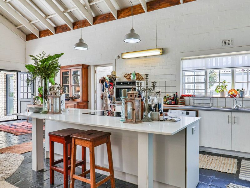 Spacious open-plan kitchen and living area featuring exposed timber rafters, white-painted brick walls, a central island, and durable stone tile flooring.