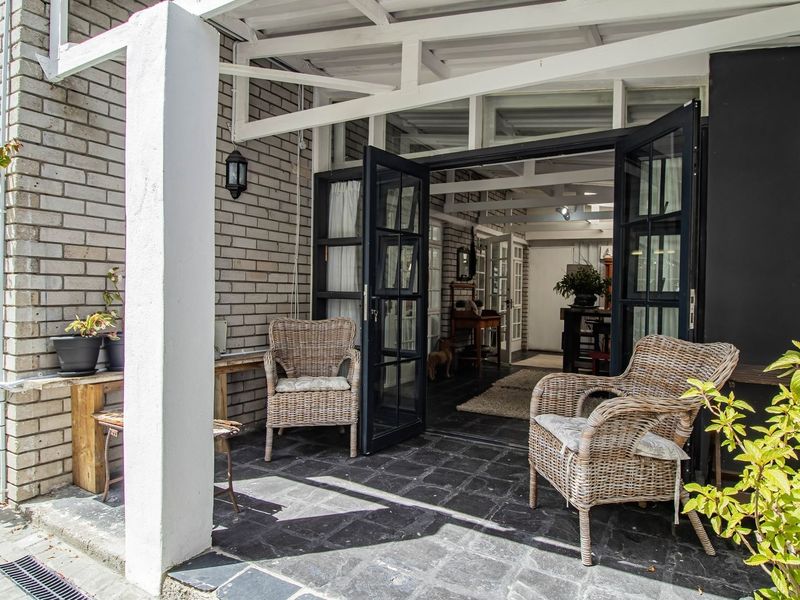 A charming covered patio featuring slate flooring, exposed white timber rafters, and classic black-framed french doors leading into the home.