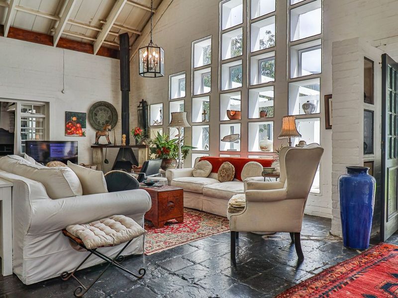 Spacious living room featuring vaulted ceilings with exposed beams, unique grid-pattern windows, a freestanding fireplace, and durable slate flooring with direct garden access.