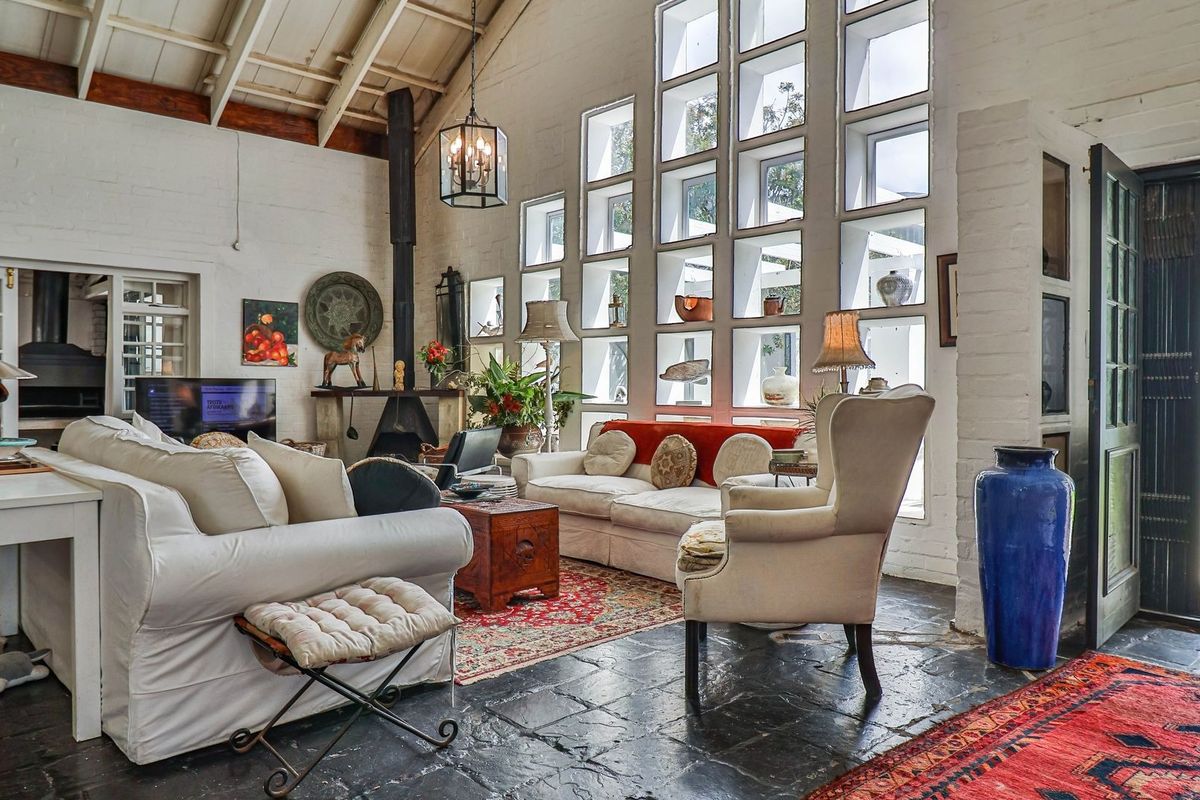 Spacious living room featuring vaulted ceilings with exposed beams, unique grid-pattern windows, a freestanding fireplace, and durable slate flooring with direct garden access.