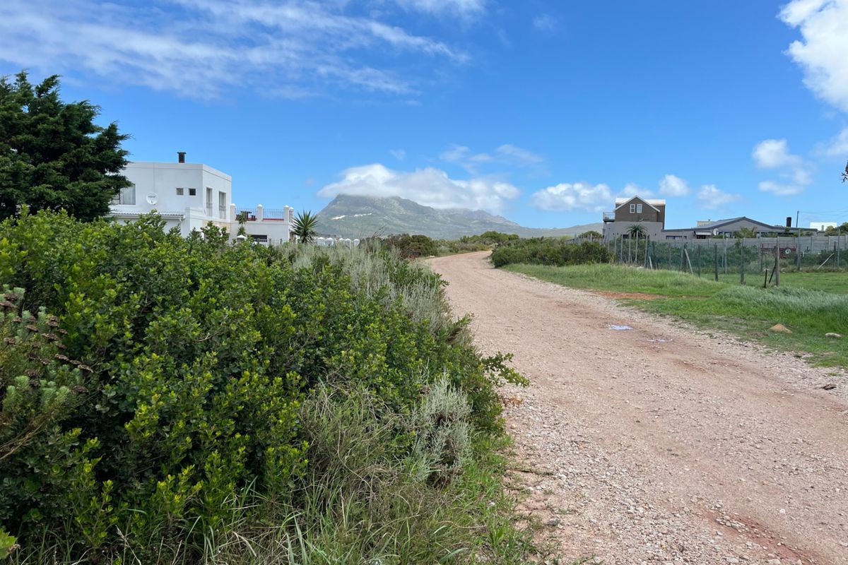 A view of an unpaved access road in a residential area, featuring surrounding indigenous vegetation and mountain views in the distance.
