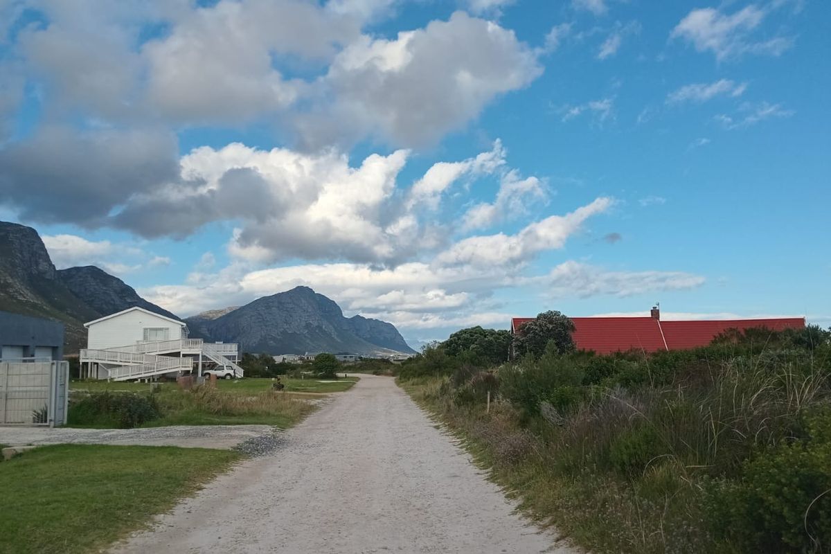 A view of a gravel access road leading through a residential area with surrounding mountain scenery and neighboring properties.