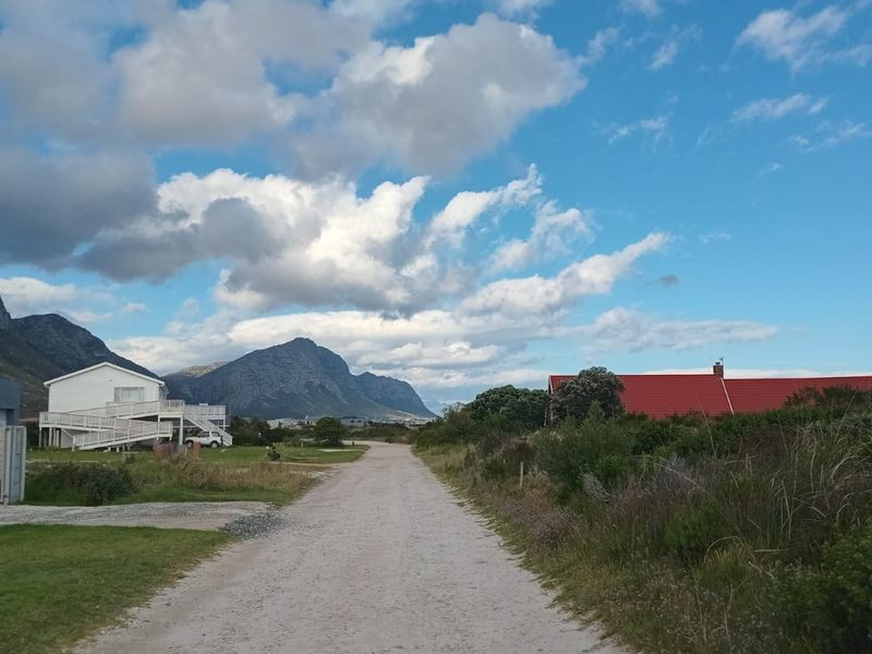 A view of a gravel access road leading through a residential area with surrounding mountain scenery and neighboring properties.