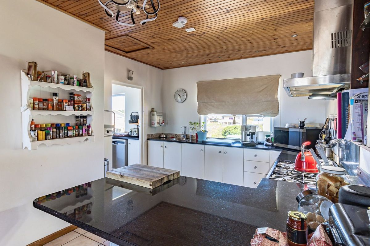 Functional kitchen featuring granite countertops, gas hob, stainless steel extractor fan, and timber tongue and groove ceiling, with an adjacent scullery area.