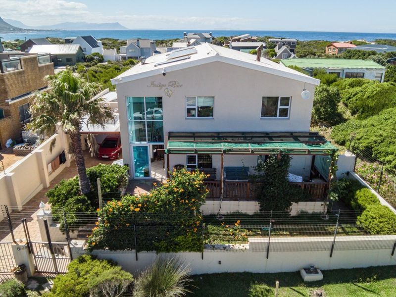 Aerial view of a double-storey coastal residence featuring a covered patio, solar water heating, and secure perimeter fencing with an established garden.