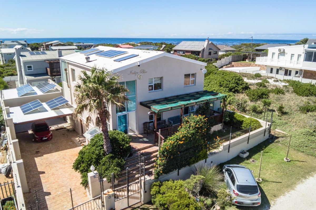 Aerial view of a coastal property featuring a multi-level home with solar panels, a paved driveway, and a covered patio area.