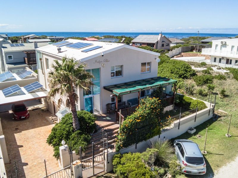 Aerial view of a coastal property featuring a multi-level home with solar panels, a paved driveway, and a covered patio area.